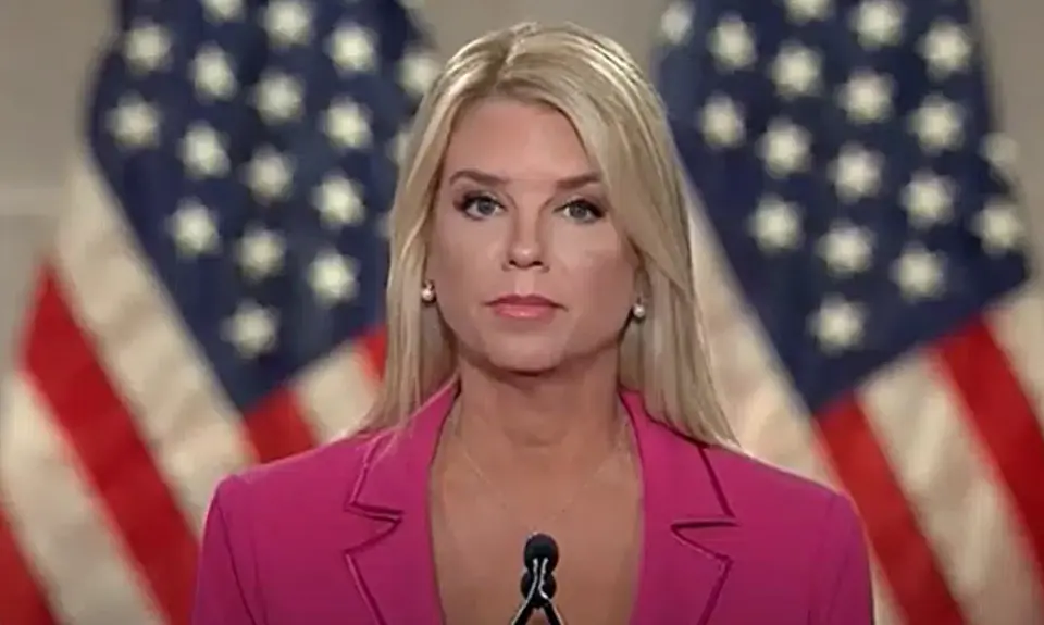 Image of Pam Bondi speaking at RNC, standing at microphone in bright pink suit with American flags visible behind her. 