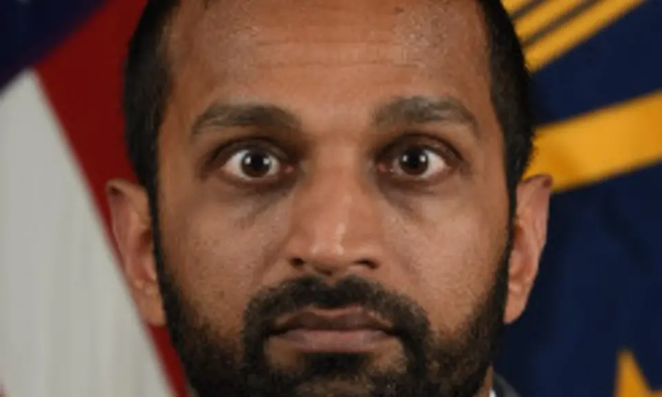 Kash Patel pictured in front of an American flag staring intensely at the camera