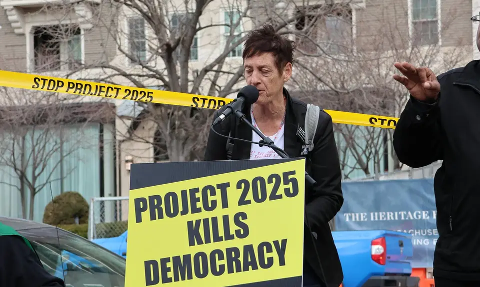 Rally speaker in front of a sign that reads "Project 2025 kills democracy"