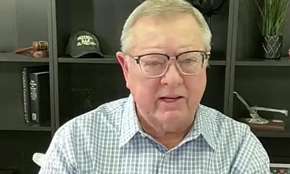 Image of Tim Sheets, a post-middle-age white man wearing glasses, sitting with bookshelf behind him  