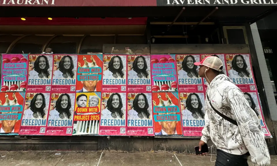 A man walks by a wall of posters of Kamala Harris that say Freedom