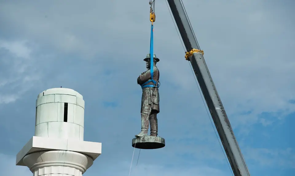 A state of Robert E. Lee is removed by a crane from its perch.