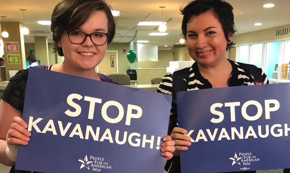 Two smiling students hold blue signs that say Stop Kavanaugh.