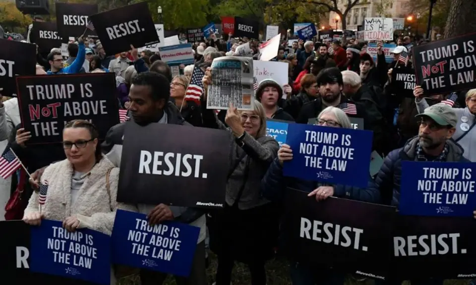 A group of people holding signs that say "Trump is not above the law" and "Resist"