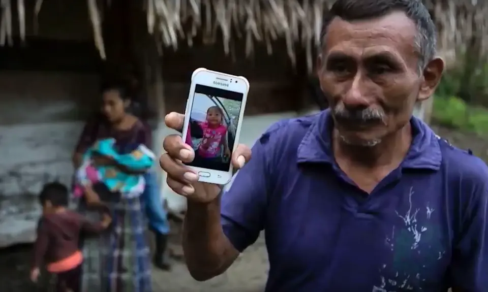 A man holds a cell phone with a picture of a young girl