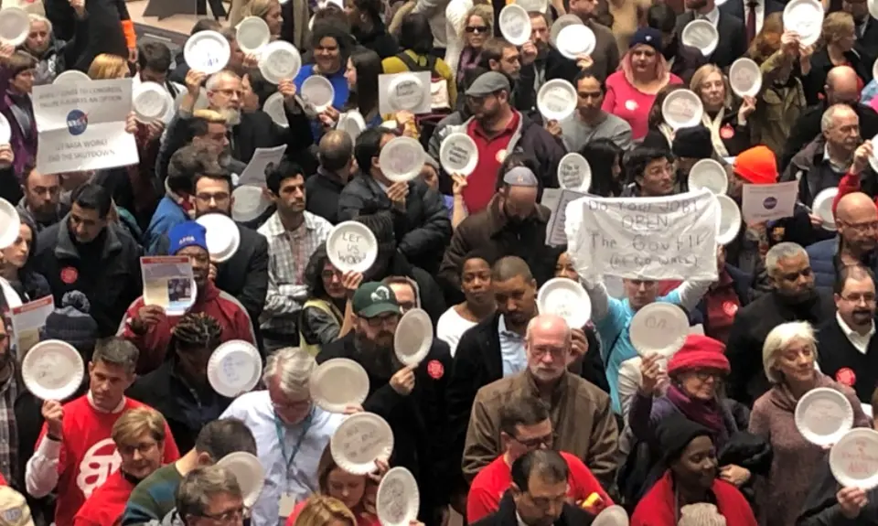 A crowd of people hold paper plates in a rally