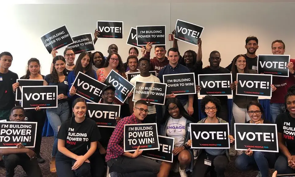 A group of people holding signs that say "Vote" and wearing tee-shirts that say "I'm building the power to win!"