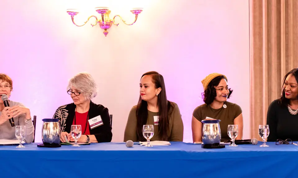 A group of multicultural women sit on a panel.