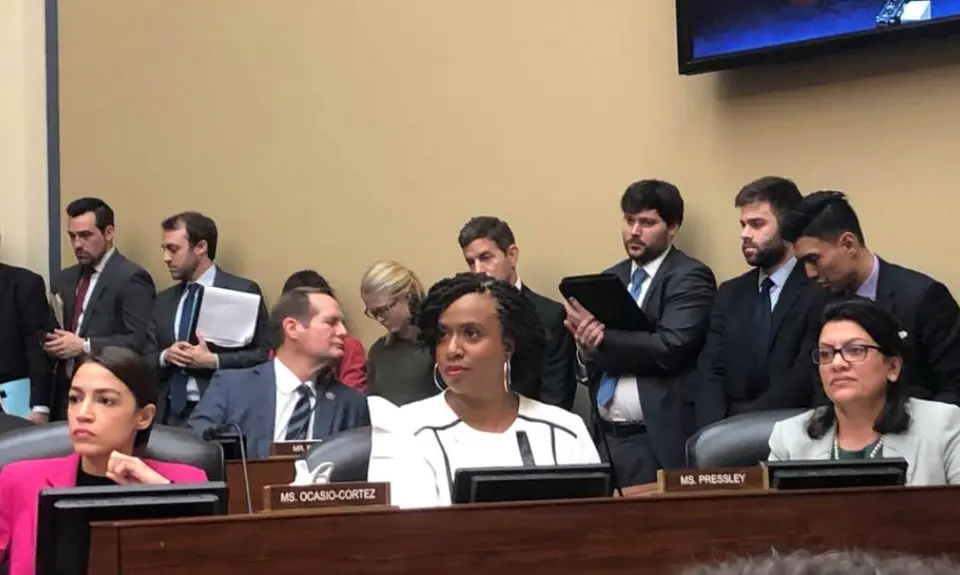 Rep. Ocasio-Cortez and Rep. Ayanna Pressley sit in a room during a hearing