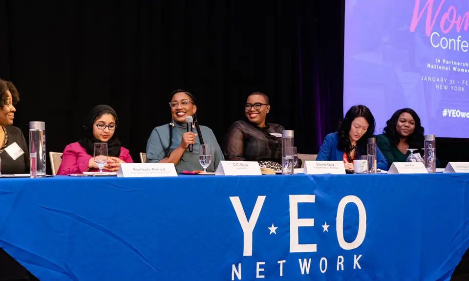 Six women sit on a panel behind a table with a banner that says "YEO Network"