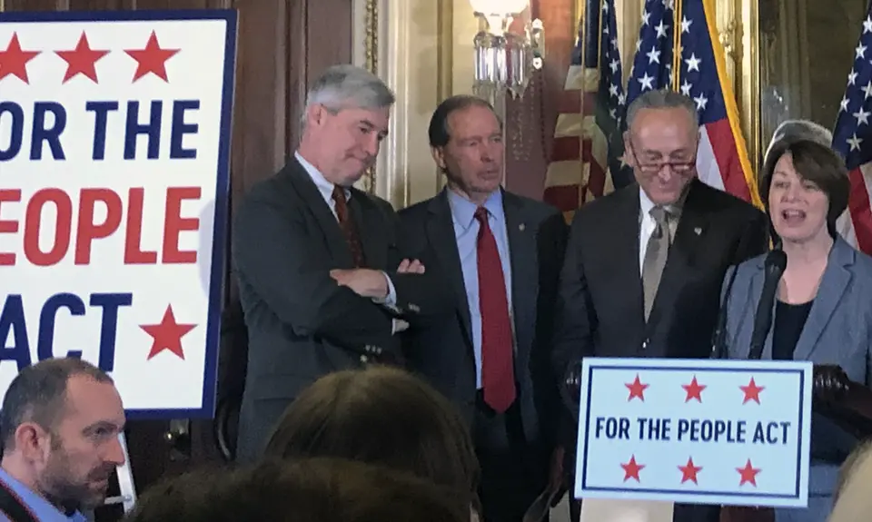 Amy Klobuchar stands at a podium next to Sens. Whiteshouse, Schumer, and Merkley to introduce the For the People Act