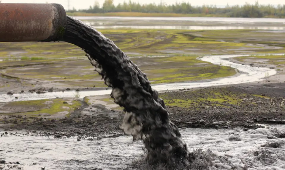 A pipe dumps grey sludge into the environment