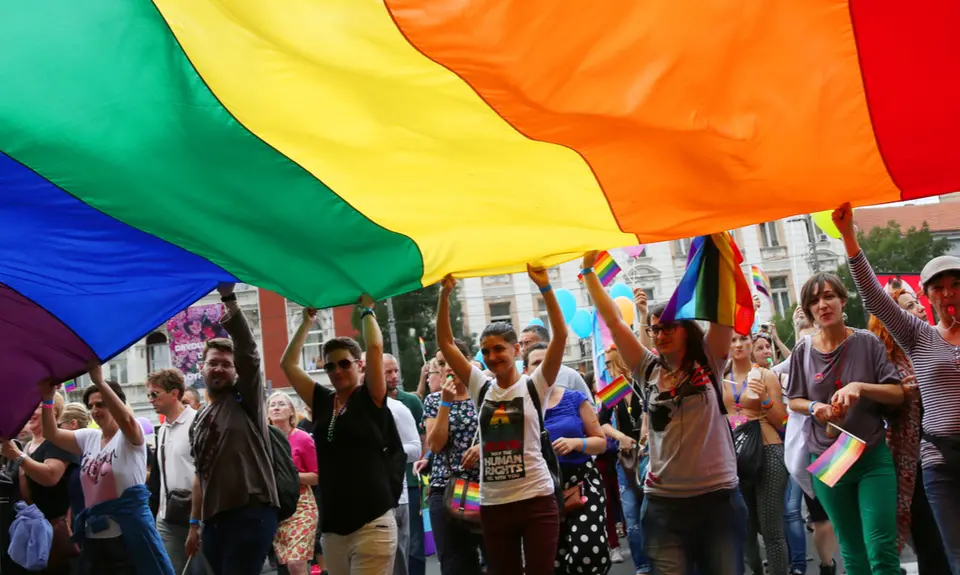 A group of people hold onto a massive rainbow flag