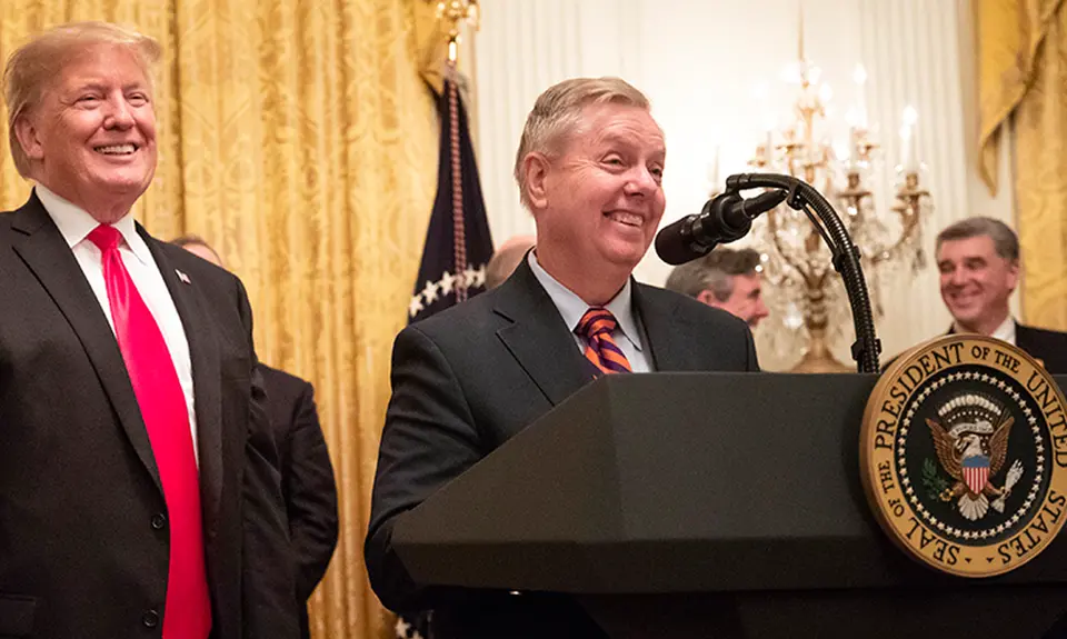 Lindsey Graham stands behind a podium with Donald Trump at his side.