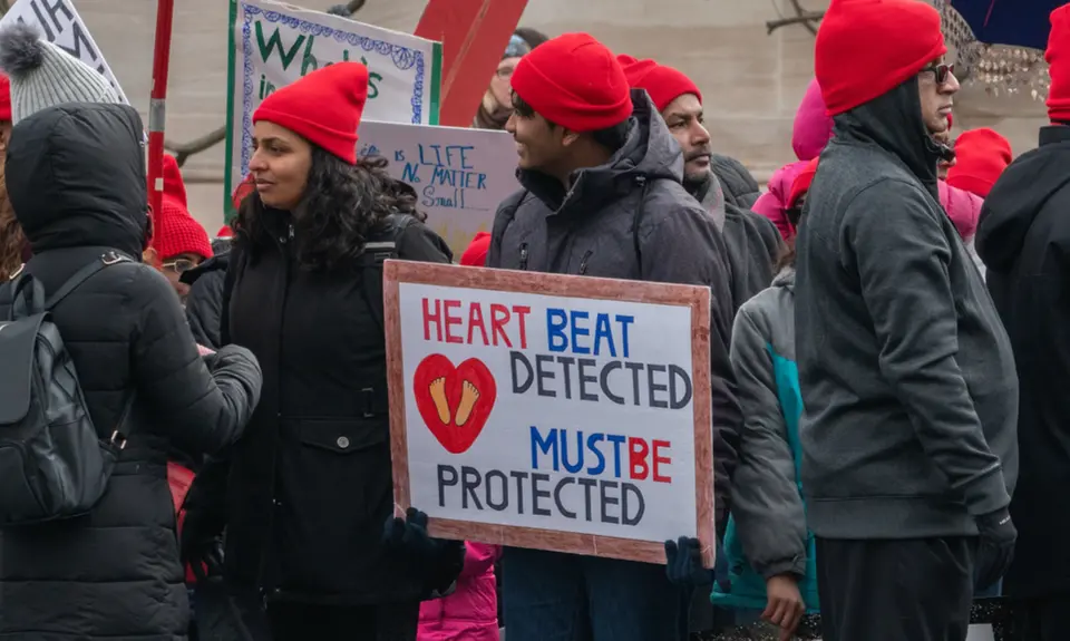 A group of anti-abortion protesters wearing red hats and holding signs that say "Heartbeat detected, must be protected"