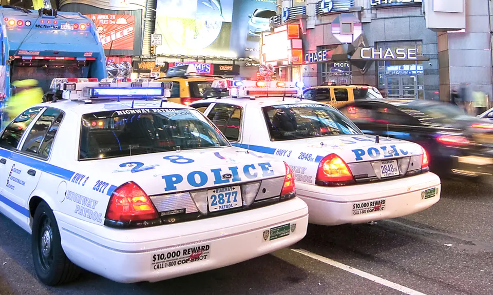 Two police cars drive side-by-side down a busy street