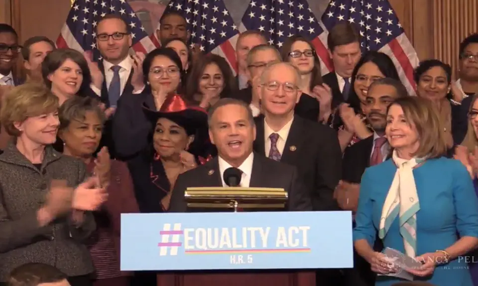 Rep. David Cicilline speaks at a podium with a group of applauding Congresspeople