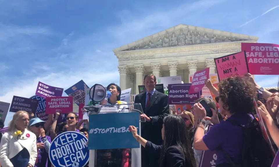 Senator Blumenthal and Representative Chu stand at a podium surround by activists at a #StoptheBans rally