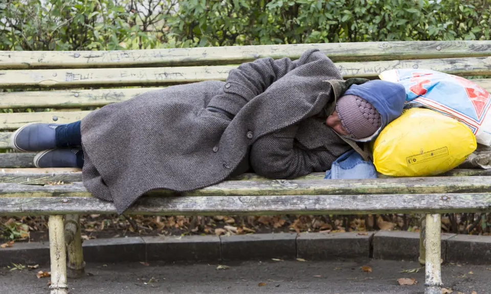 A homeless person naps with their belongings on a bench