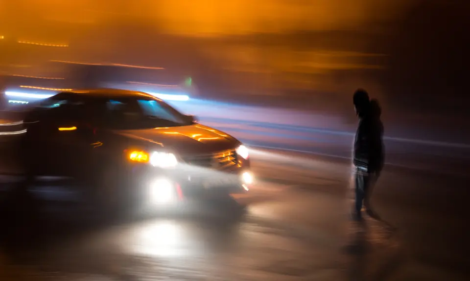 A person crosses the street in front of a car.