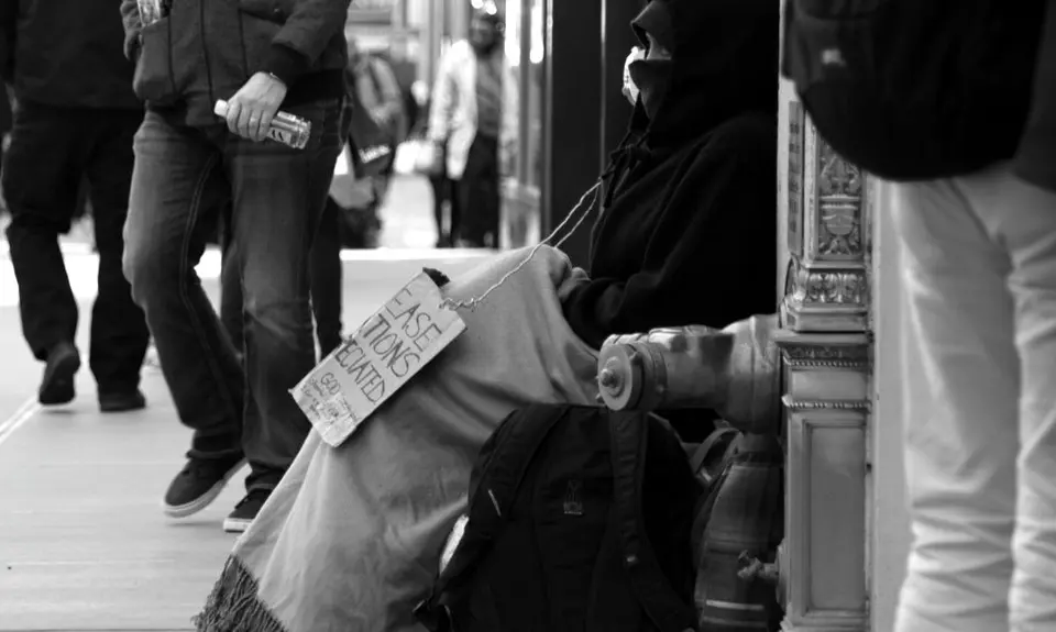 homeless man sitting on street with sign