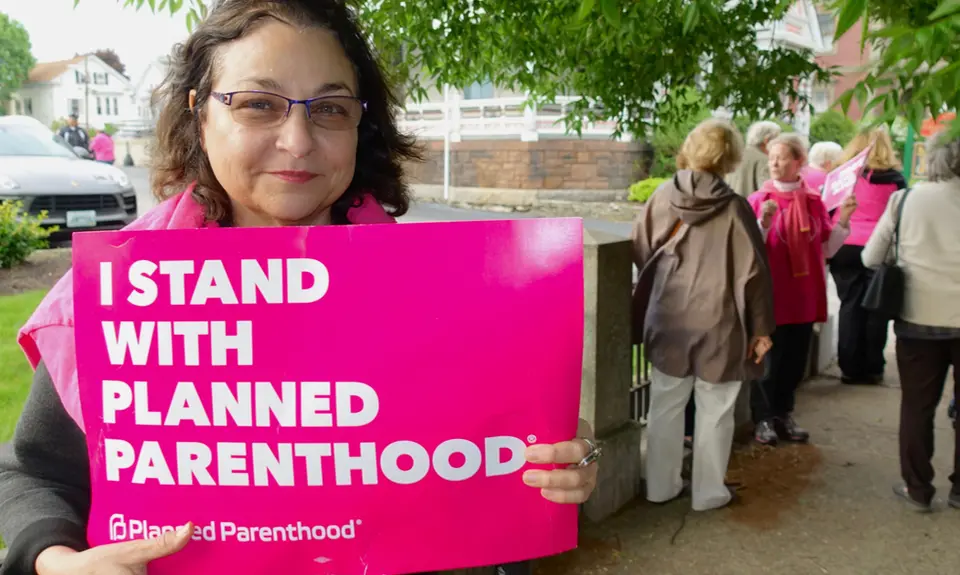 A woman holds a pink sign that says "I stand with Planned Parenthood"