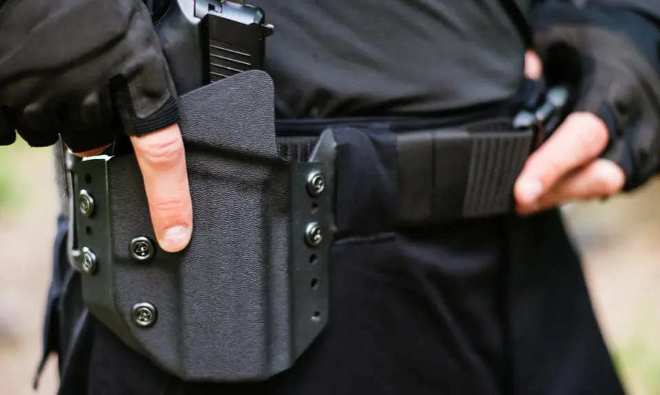 A close up of a police officer's belt; the officer has his hand on his gun