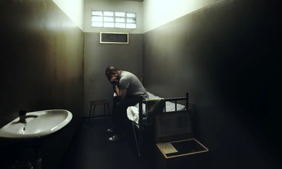 A man in solitary confinement sits on his bed in a small cell.