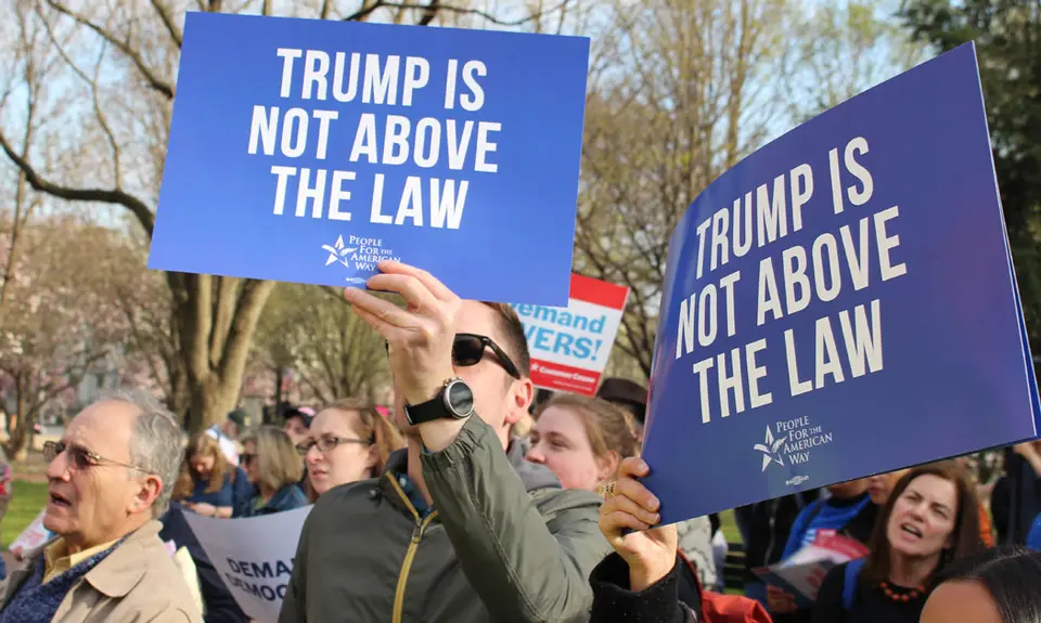 Activists hold signs saying "Trump is not above the law."