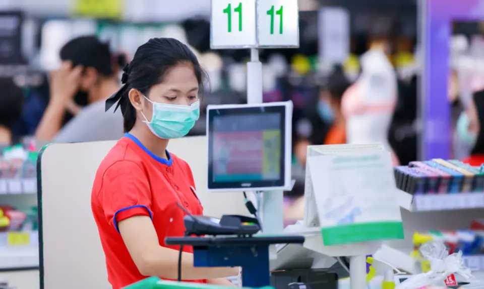 A young grocery store cashier wears a surgical mask while she works.