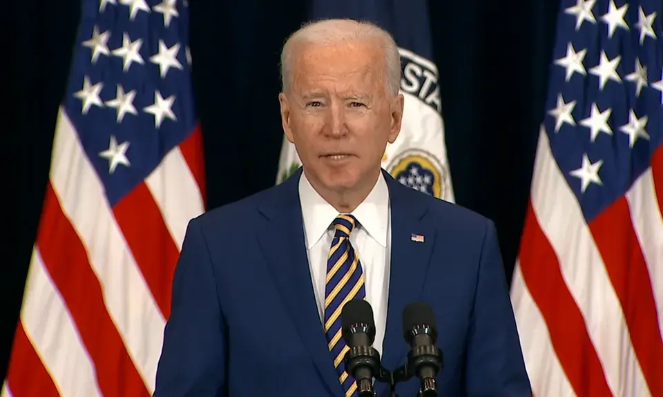 President Joe Biden stands in front of several American flags.