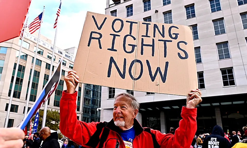 A man holds a cardboard sign that reads Voting Rights Now