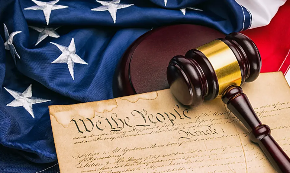 Picture of an American Flag and the U.S. Constitution with the phrase "We The People" clearly visible underneath a gavel.