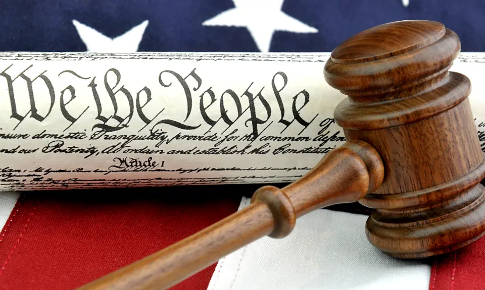 Picture of an American Flag and the U.S. Constitution with the phrase "We The People" clearly visible underneath a gavel.