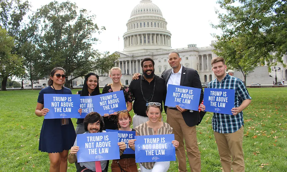 A group of people hold signs saying "Trump is not above the law" with the Capitol in the background.