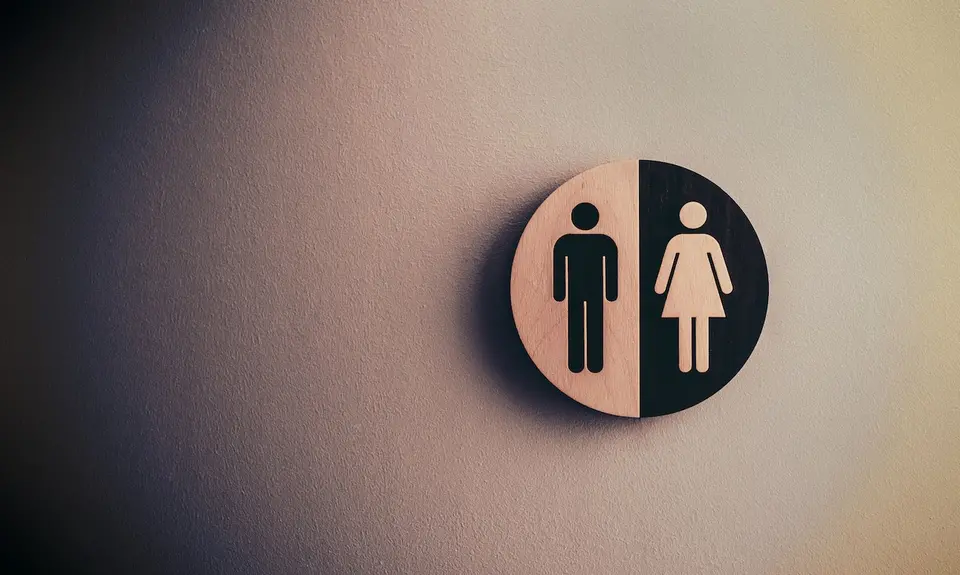 A white wall with a sign showing man and woman symbols seen outside public bathrooms.