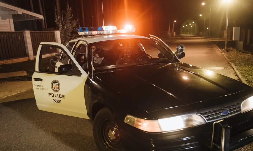 A photo of two police officers in a police car with one person in the back seat.