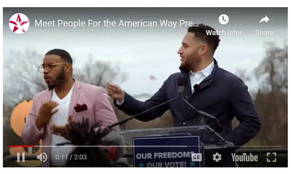 A still of Svante Myrick speaking at a podium with a sign language interpreter next to him.