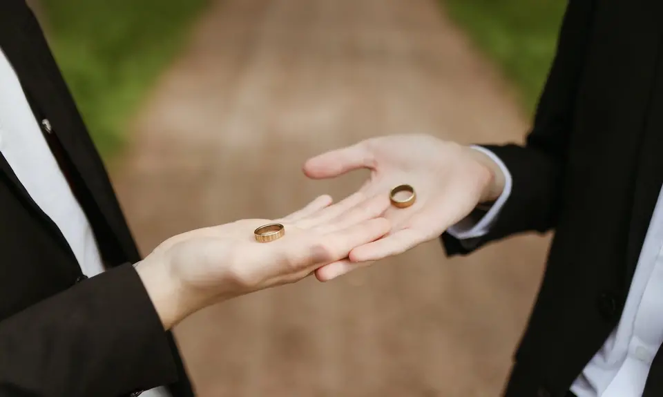 Two hands each holding a wedding ring in their palms.