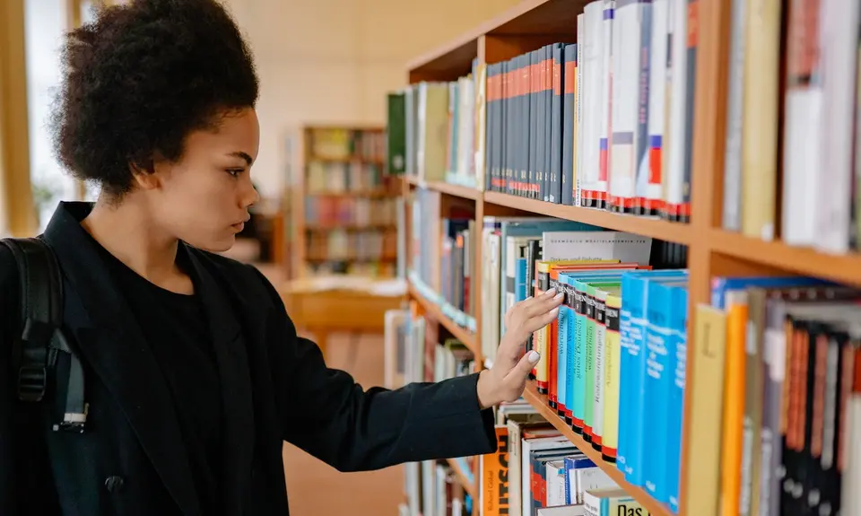 A Black woman looks at a shelf of books in a school library.