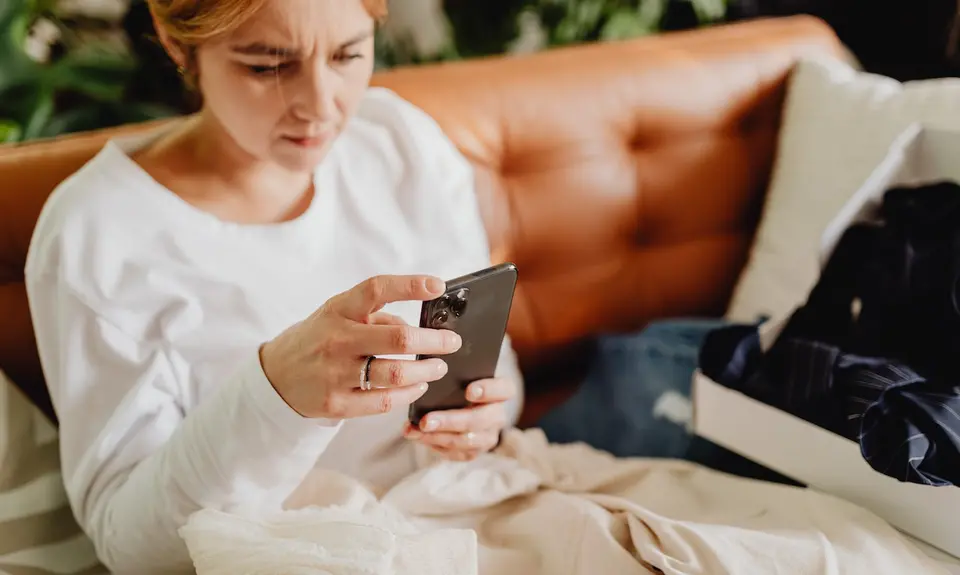 A woman sits on a sofa glaring at her phone.