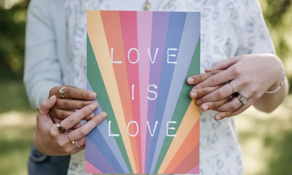 Two people holding a book with "Love is love" and a rainbow design on the cover.