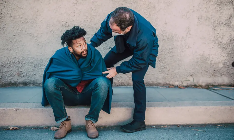 A public safety officer helps a man sitting on a curb.