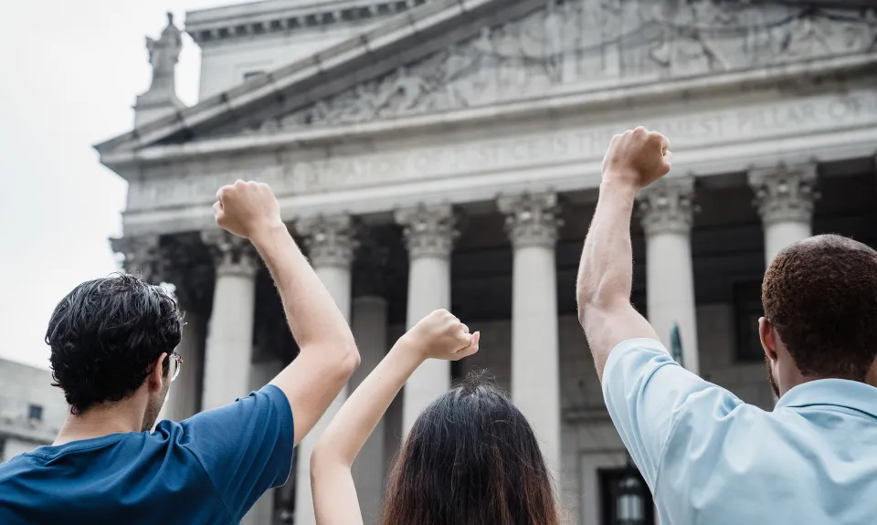 Three people raise their fists outside the Supreme Court building.