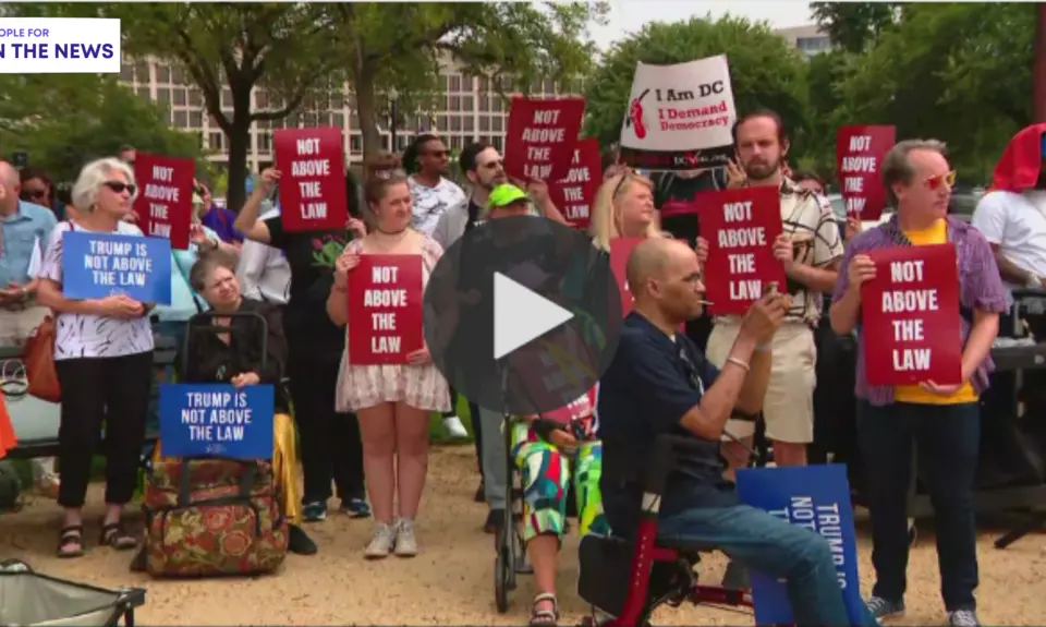 A group of people standing outside holding signs that read "Not Above the Law"