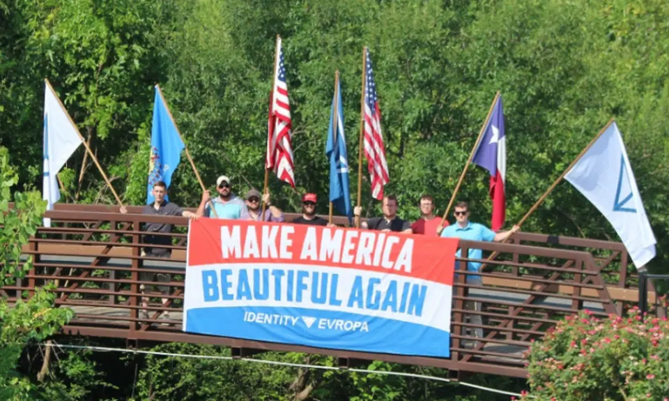 A group of white nationalists holding flags on a bridge.