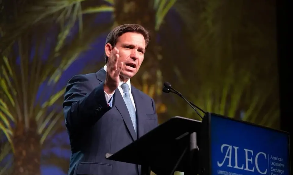 Ron DeSantis standing in front of a podium that says "ALEC" on it.