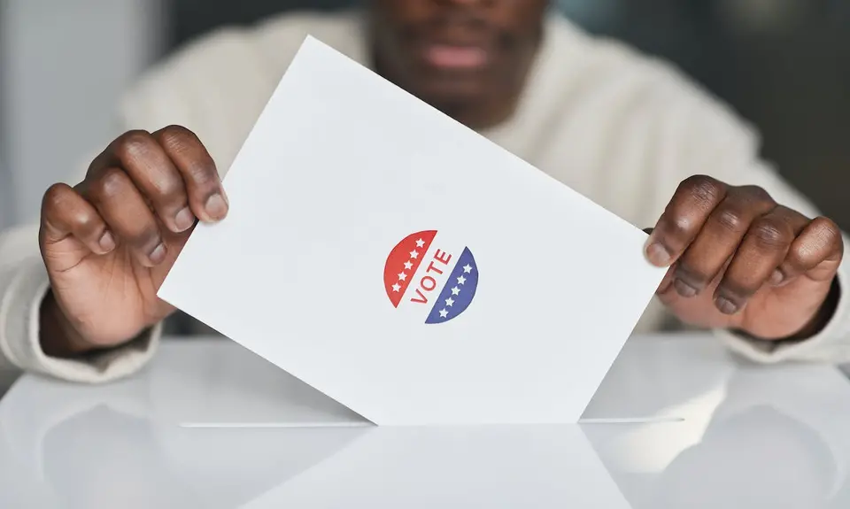 Two hands holding a piece of paper with a sticker that says "Vote"