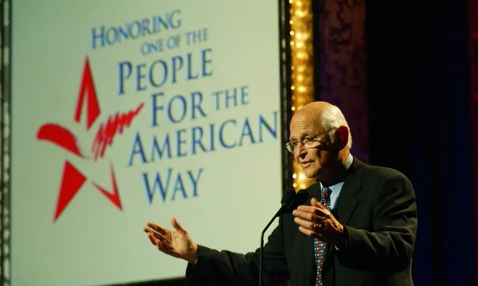 Norman Lear at a podium in front of a sign that reads "People For the American Way"