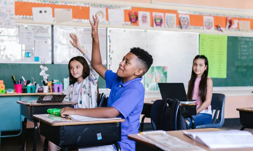 A Black child raising their hand in a classroom